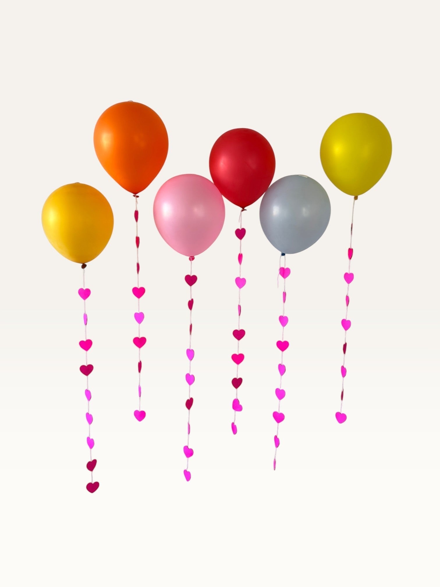 Paper Party Studio heart garland strings with pink paper hearts hanging from colorful party balloons