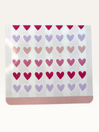 Paper Party Studio heart sticker sheet with rows of glossy pink, red, and lilac heart stickers on a striped background.