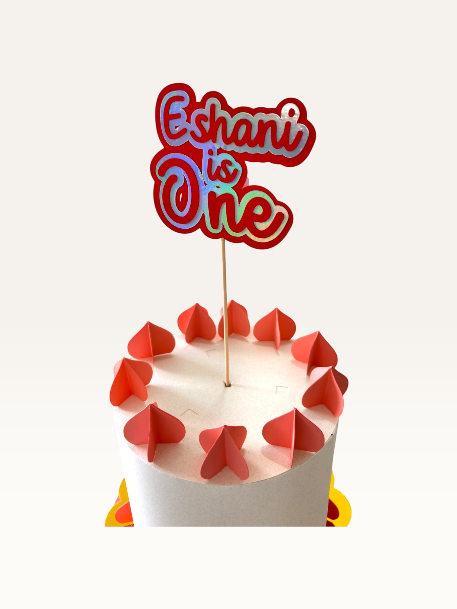 Paper Party Studio personalised holographic script cake topper reading Eshani is One on a decorative birthday cake.