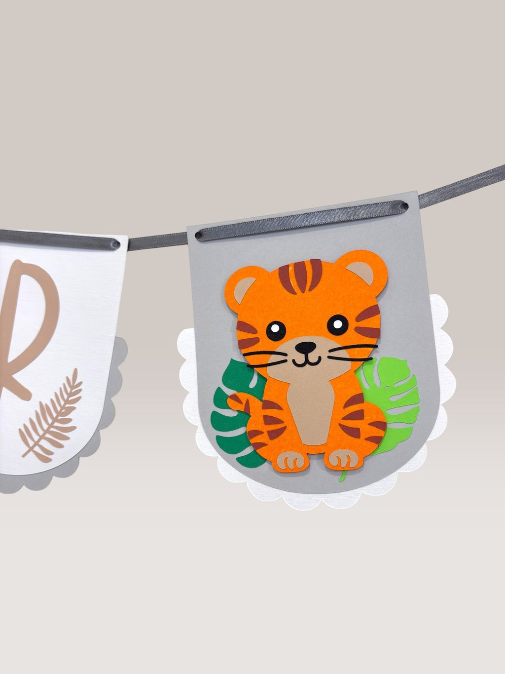 Paper Party Studio jungle birthday banner with a cute tiger, green leaves, and scalloped edges. White flags with kraft lettering.