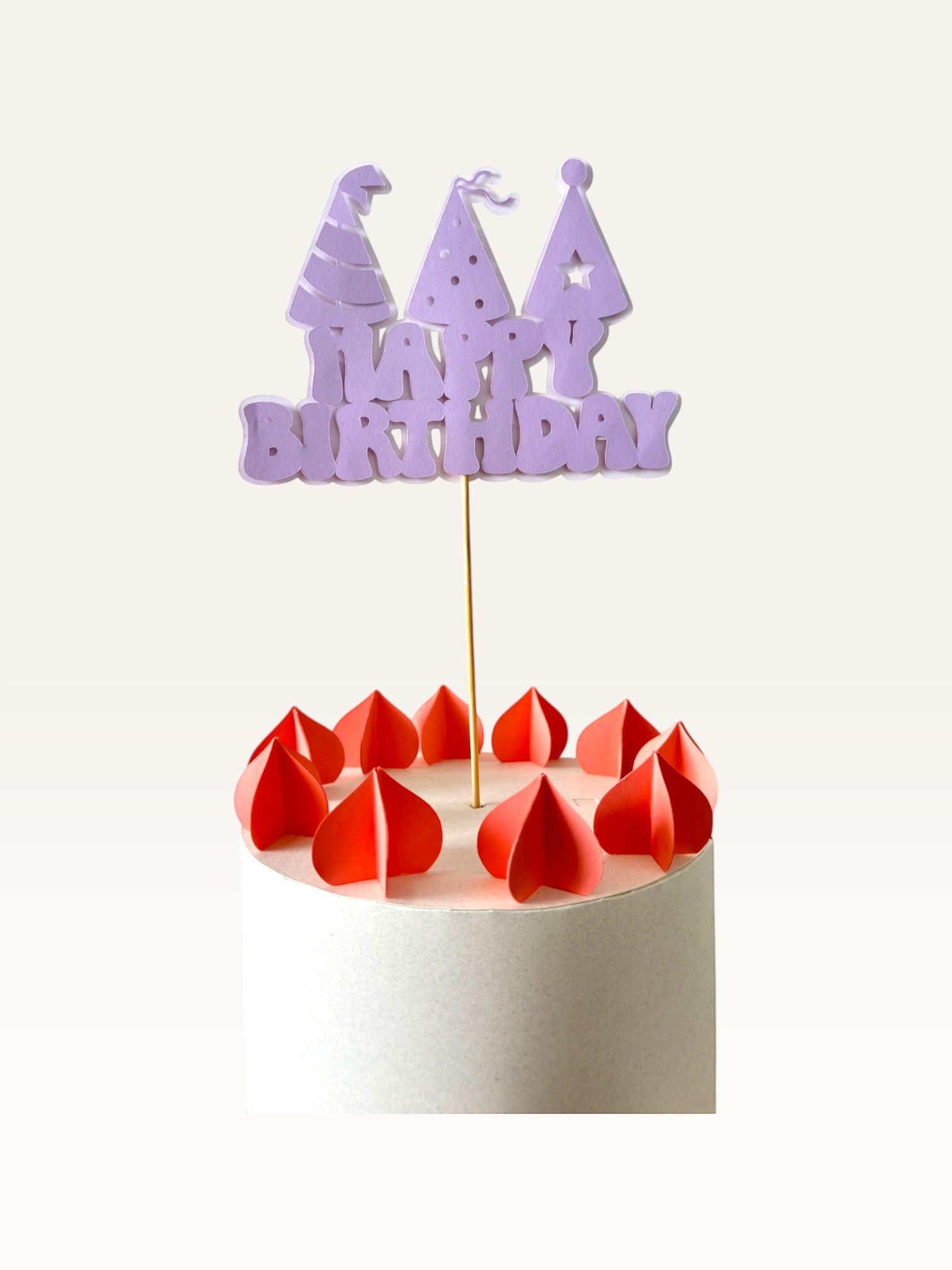 Paper Party Studio lavender Happy Birthday cake topper with party hat cut-outs on a wooden pick atop a white cake.