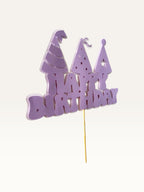 Paper Party Studio lavender Happy Birthday cake topper with three party hat cut-outs on a wooden pick