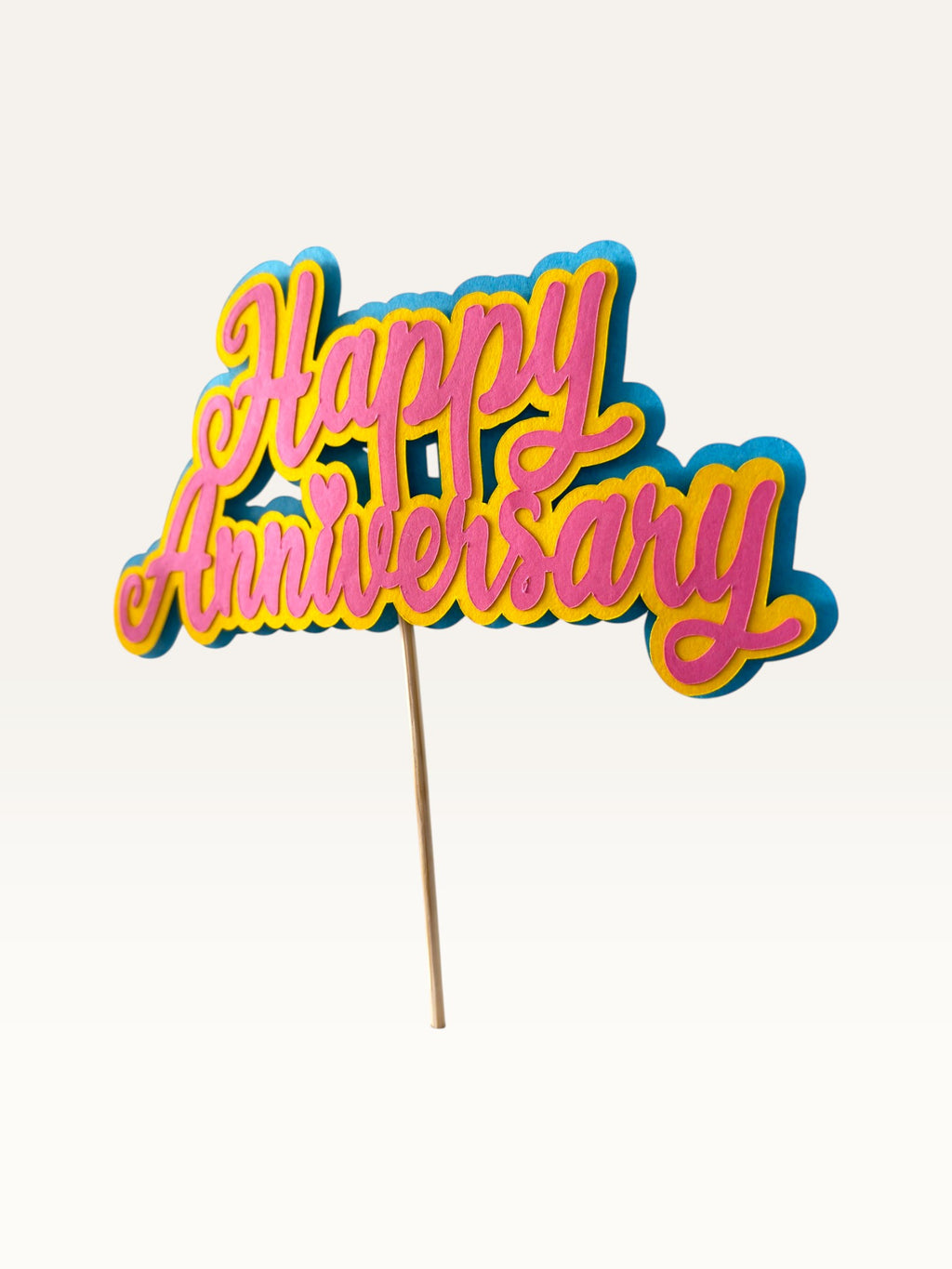 Paper Party Studio layered cardstock Happy Anniversary cake topper in pink, yellow, and blue script with a heart detail.