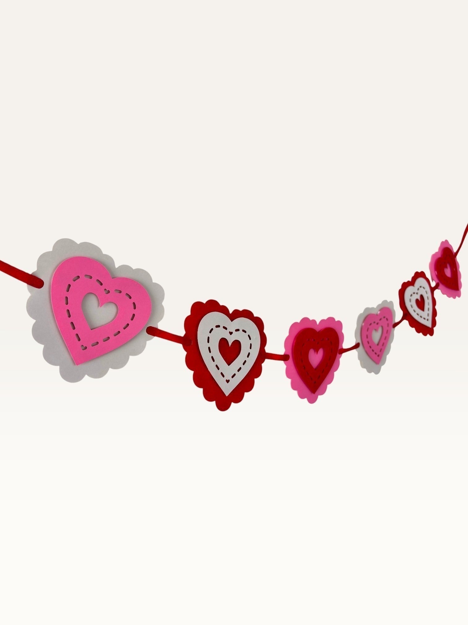 Paper Party Studio layered heart garland with pink, red, and white scalloped cardstock hearts and stitched details.