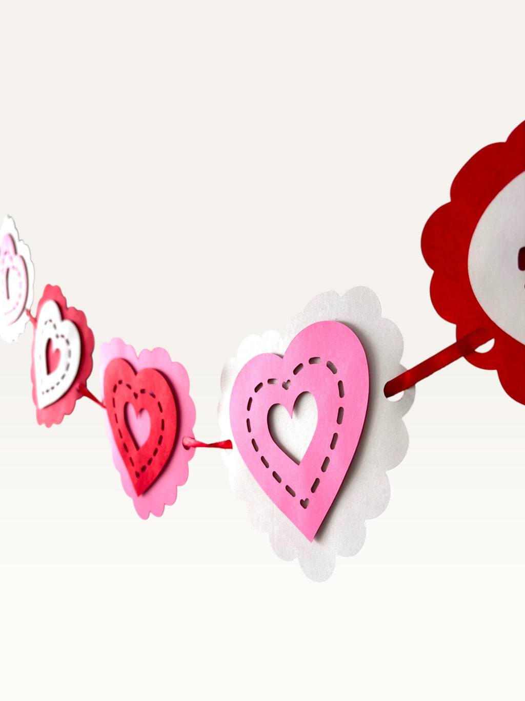 Paper Party Studio layered heart garland featuring scalloped pink, red, and white cardstock hearts with stitched detail.