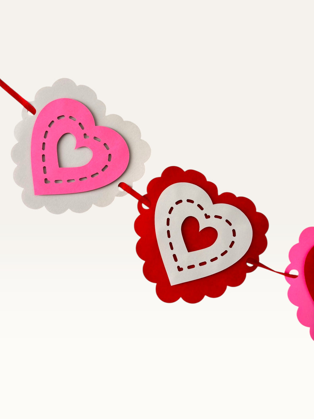 Paper Party Studio layered heart garland with scalloped pink, red, and white cardstock hearts and stitched details.