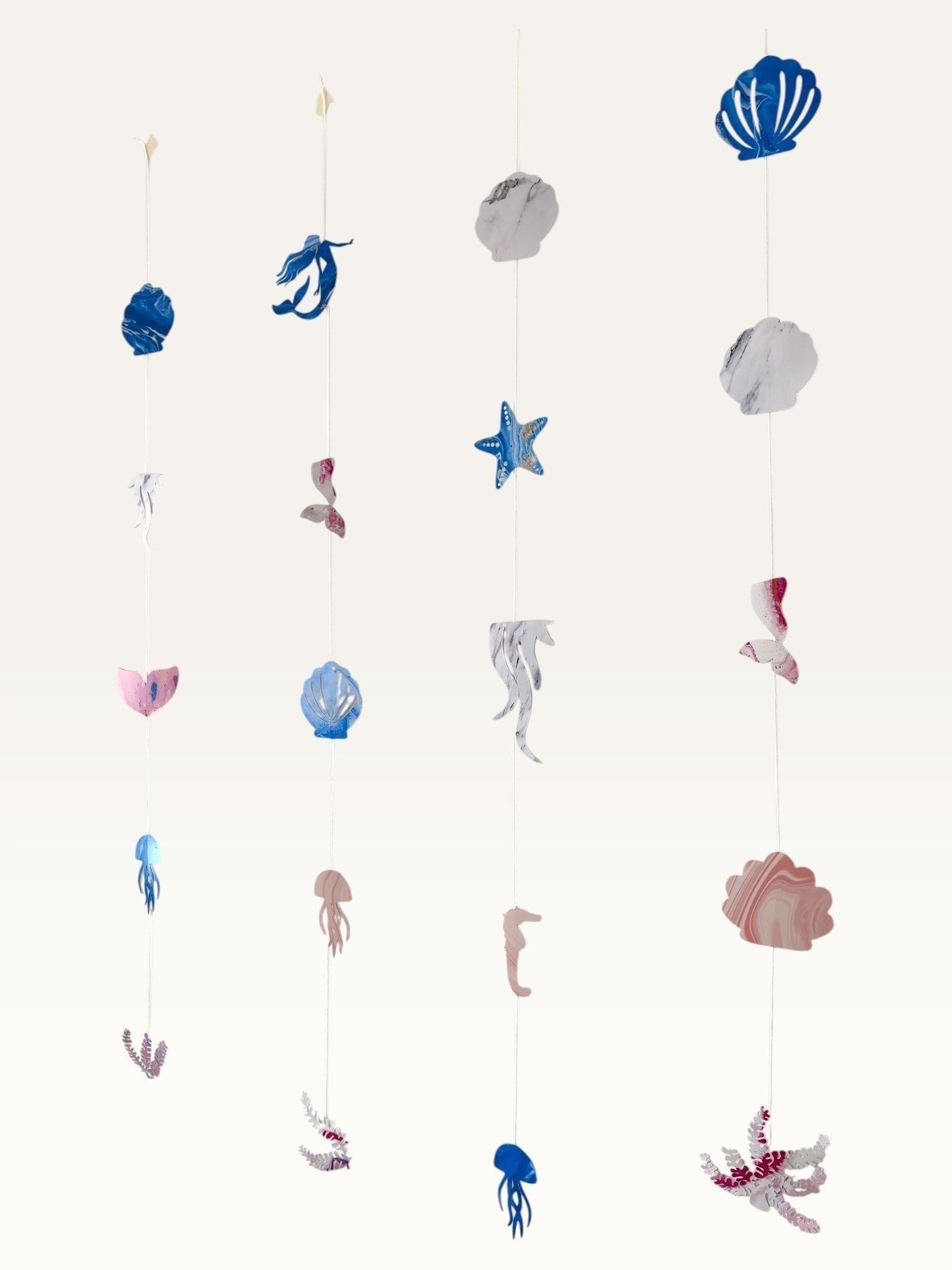 Paper Party Studio under the sea hanging backdrop with cardstock mermaid tails, shells, and seahorses in pink and blue.