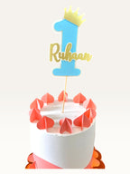 Paper Party Studio personalized blue number one cake topper with a gold crown and name on a decorated cake