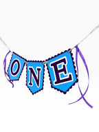 Paper Party Studio blue scalloped banner spelling ONE with purple ribbon ties, perfect for a first birthday cake smash.