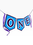 Paper Party Studio blue scalloped banner spelling ONE with purple ribbon ties, perfect for a first birthday cake smash.