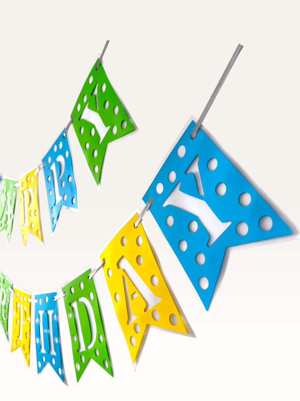 Paper Party Studio Happy Birthday banner with blue, green, and yellow polka dot swallowtail flags and white letters.