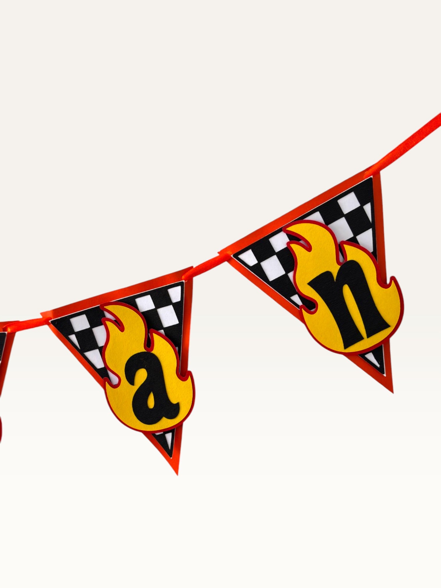 Paper Party Studio personalised racing name banner with checkered flag pennants and yellow flame letter cutouts.