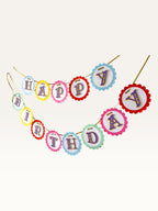 Paper Party Studio rainbow scalloped Happy Birthday banner with purple and gold lettering on a gold ribbon.