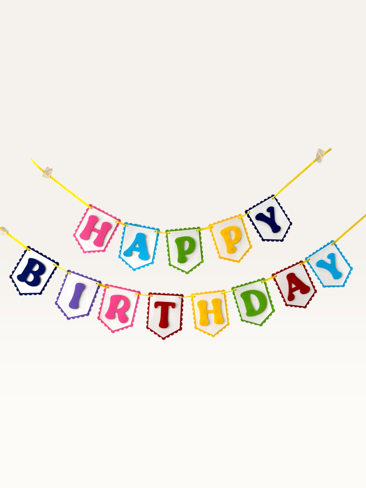 Paper Party Studio rainbow Happy Birthday banner with scalloped white paper flags on a yellow cord.