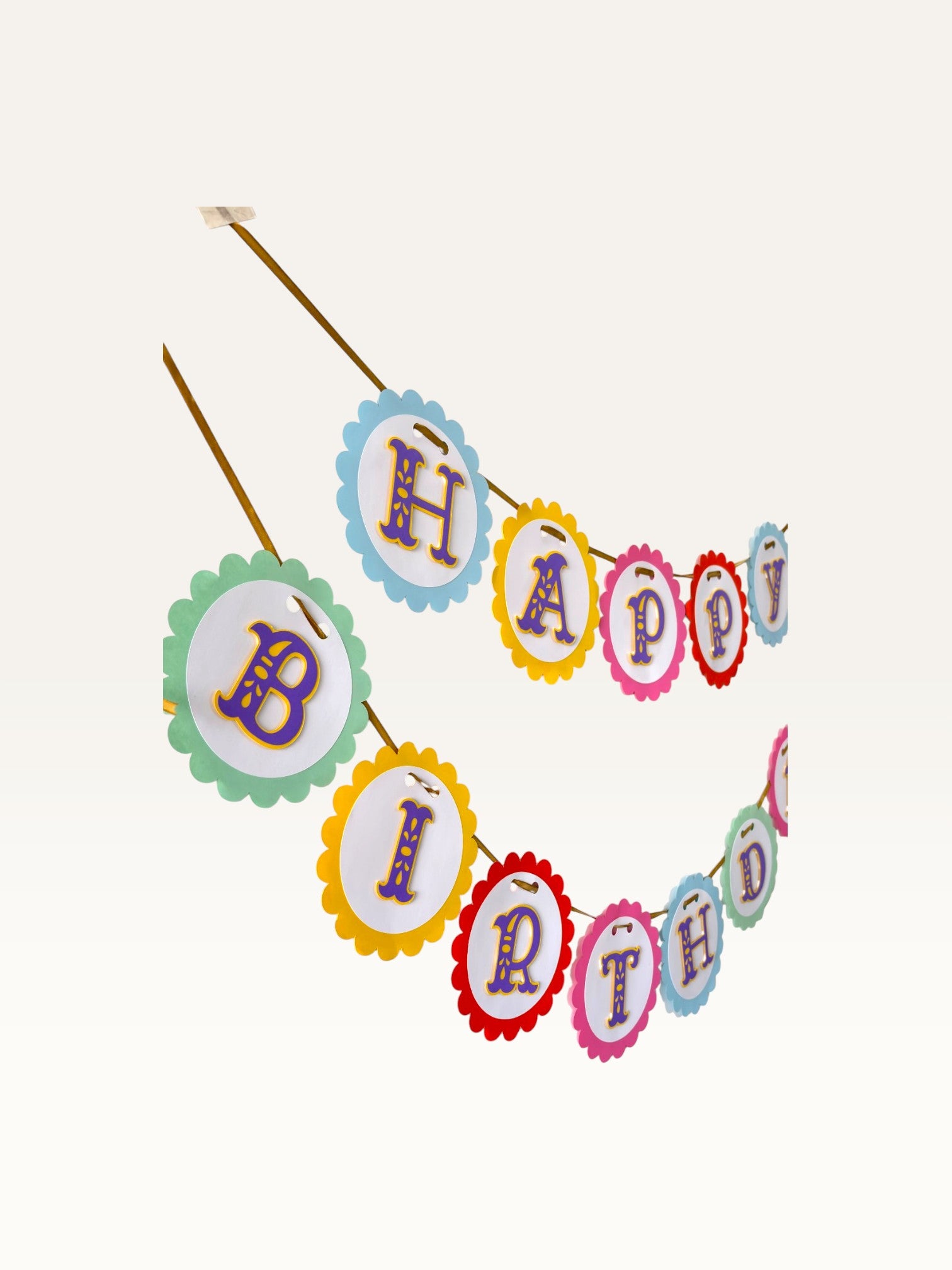 Paper Party Studio rainbow scalloped Happy Birthday banner with purple and gold ornate lettering on a gold ribbon.