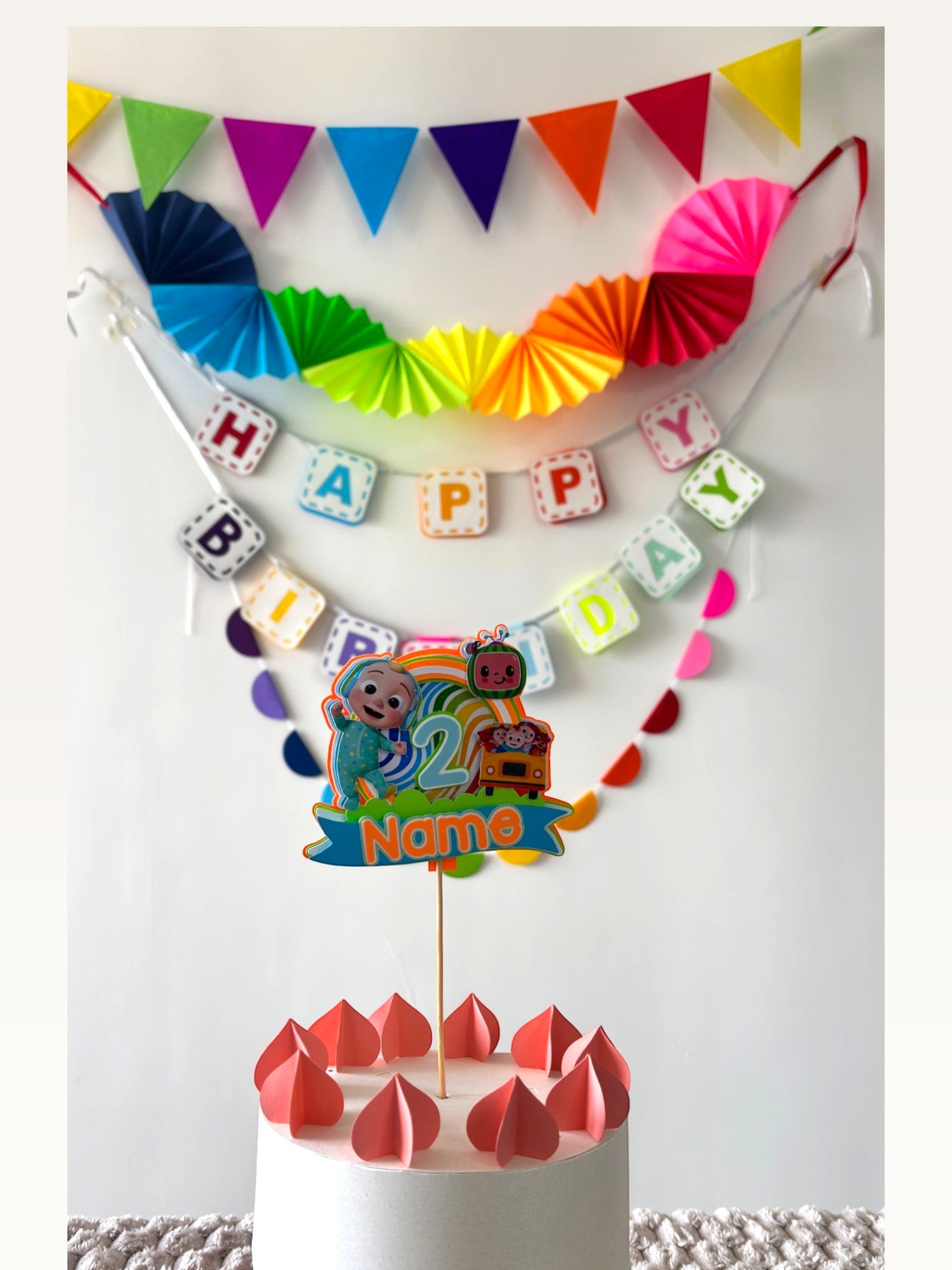 Paper Party Studio rainbow birthday decoration set with Cocomelon cake topper, paper fans, bunting, and banner.