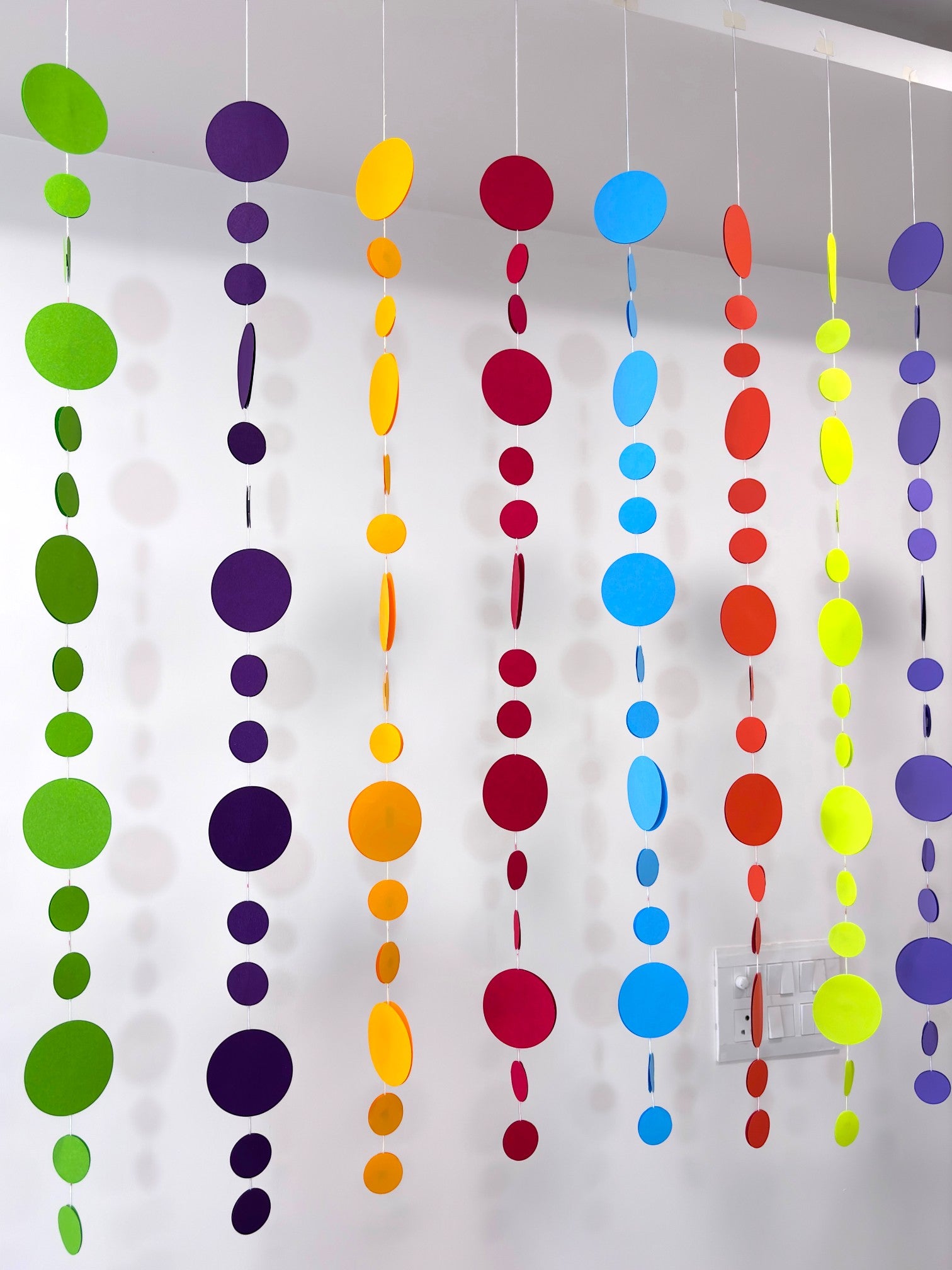 Paper Party Studio rainbow circle garland with graduated paper dots in bright colours, strung on white thread.