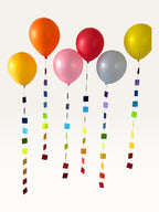 Paper Party Studio rainbow square paper garland strings hanging as colourful balloon tails for party decorations.