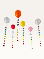 Paper Party Studio rainbow square garland strings hanging as colourful balloon tails for party decoration.