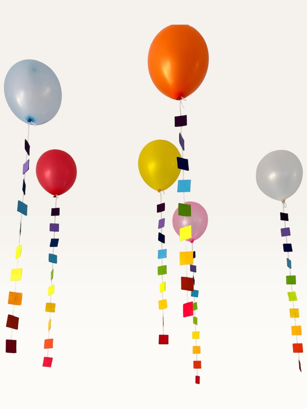 Paper Party Studio rainbow square garland strings hanging as colourful balloon tails for party decoration.