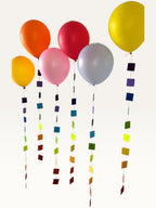 Paper Party Studio rainbow square paper garland strings hanging as colourful balloon tails for party decoration.