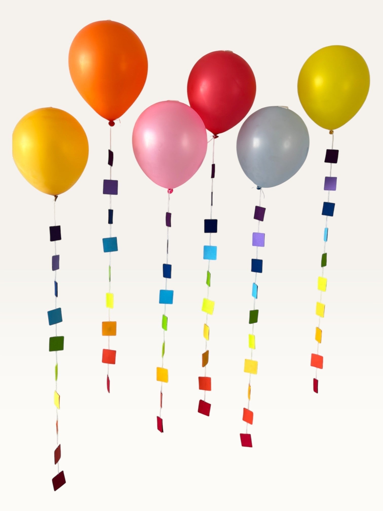 Paper Party Studio rainbow square paper garland strings hanging as colourful balloon tails for party decoration.