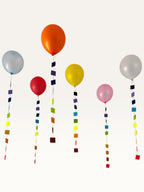Paper Party Studio rainbow square garland strings hanging from colourful balloons for a festive party decoration.