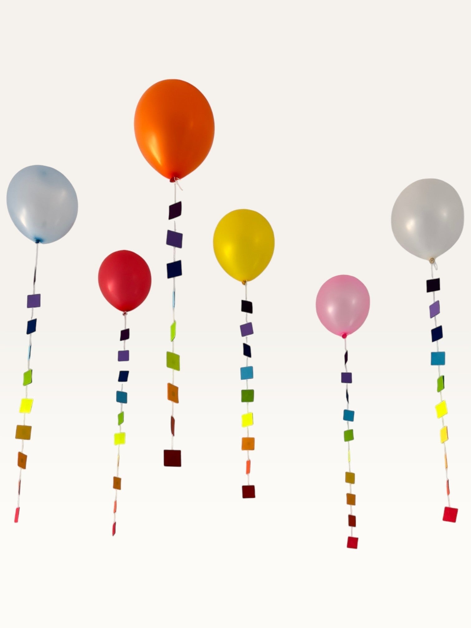 Paper Party Studio rainbow square garland strings hanging from colourful balloons for a festive party decoration.