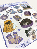 Paper Party Studio Rainy Day sticker sheet with glossy illustrations of a yellow raincoat, sleeping cat, and cozy items.