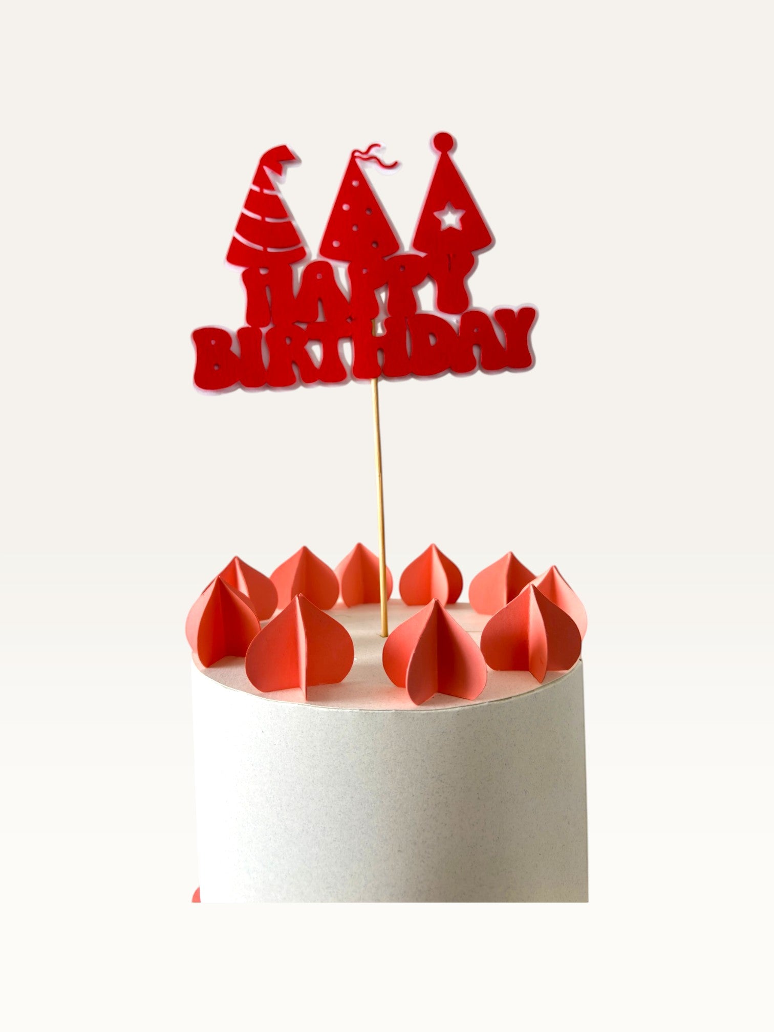 Paper Party Studio red Happy Birthday cake topper with party hat cut-outs on a white cake with paper decorations.