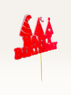 Paper Party Studio red Happy Birthday cake topper with three party hat cut-outs on a wooden pick.