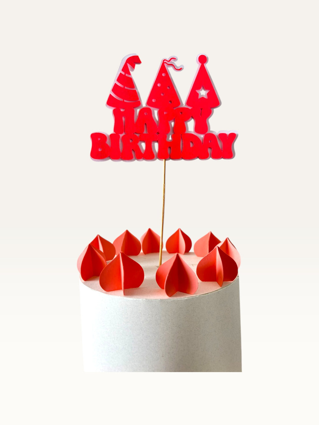 Paper Party Studio red Happy Birthday cake topper with three party hats on a wooden pick atop a white cake