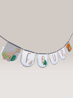 Paper Party Studio safari birthday banner with white scalloped flags spelling "FOUR", featuring a giraffe and tiger, and tropical leaves.