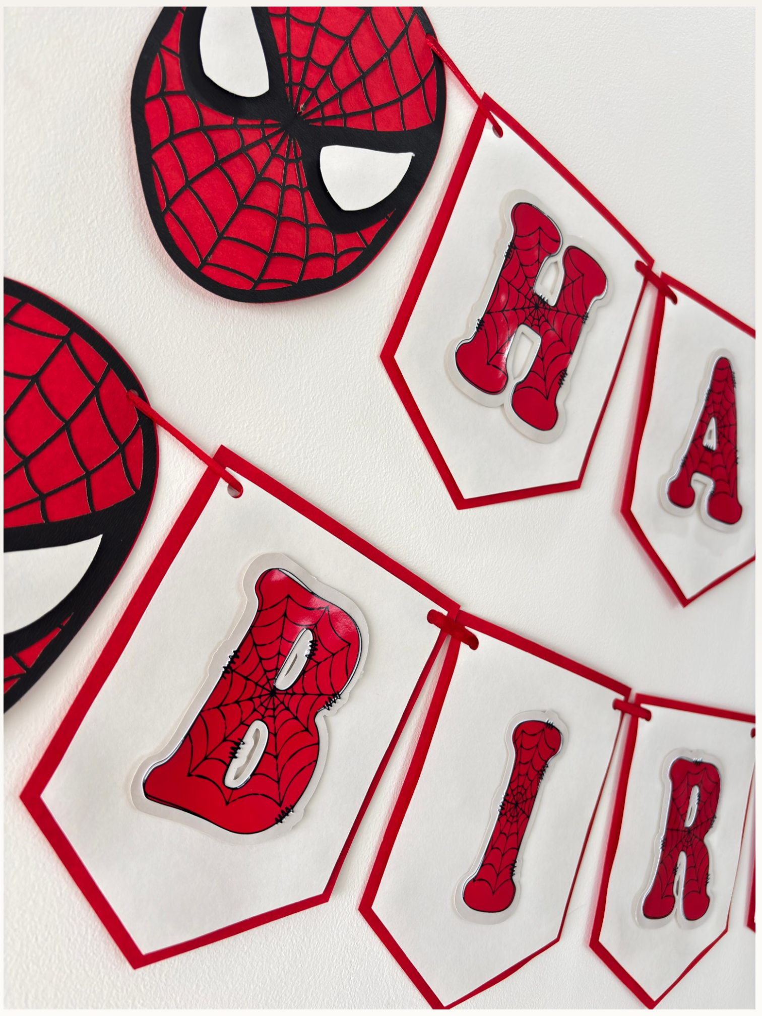 Paper Party Studio red and white swallowtail birthday banner with black spider-web lettering and hero mask accents.