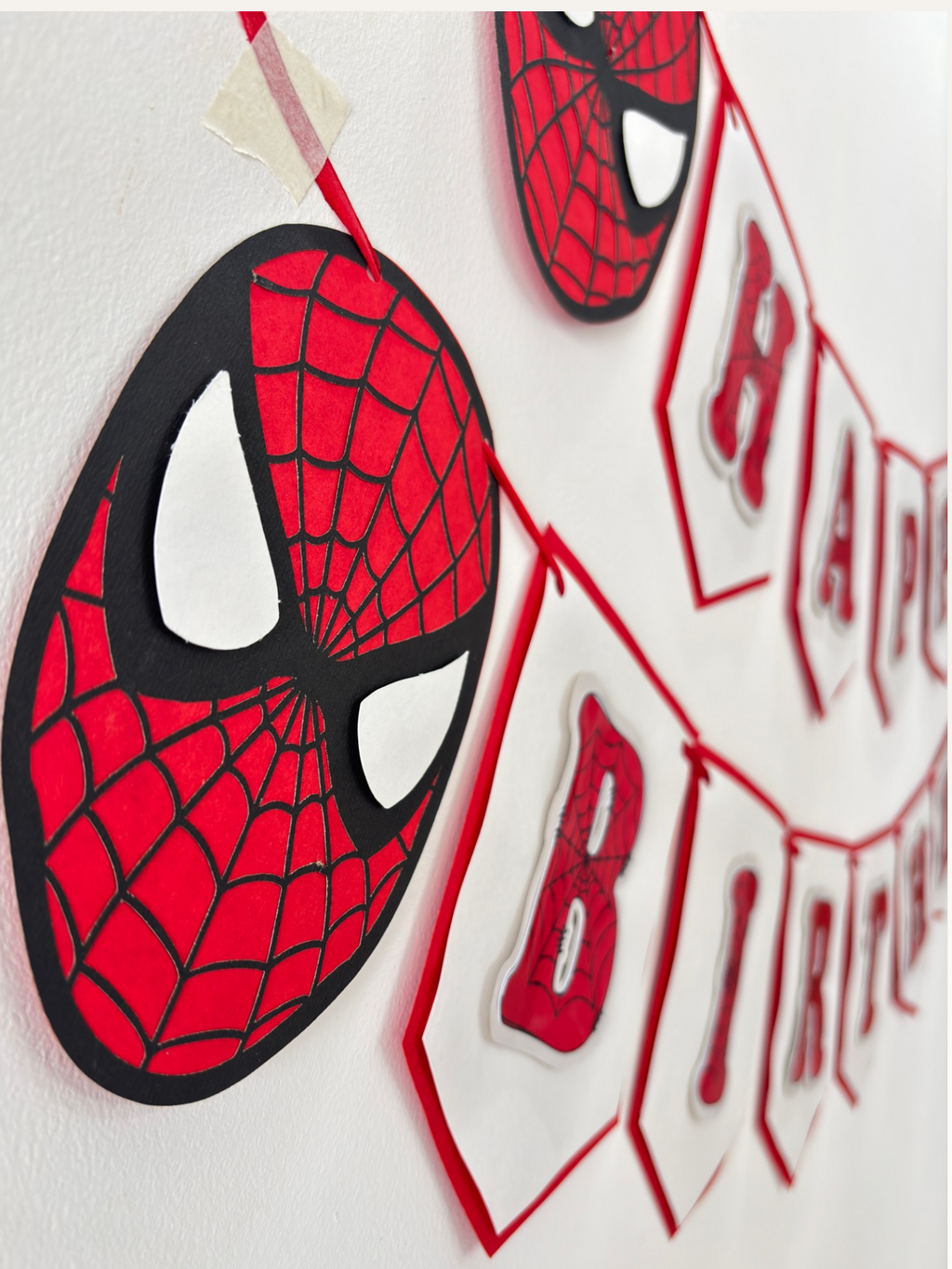 Paper Party Studio red and black spider-web Happy Birthday banner with masked hero face medallions.