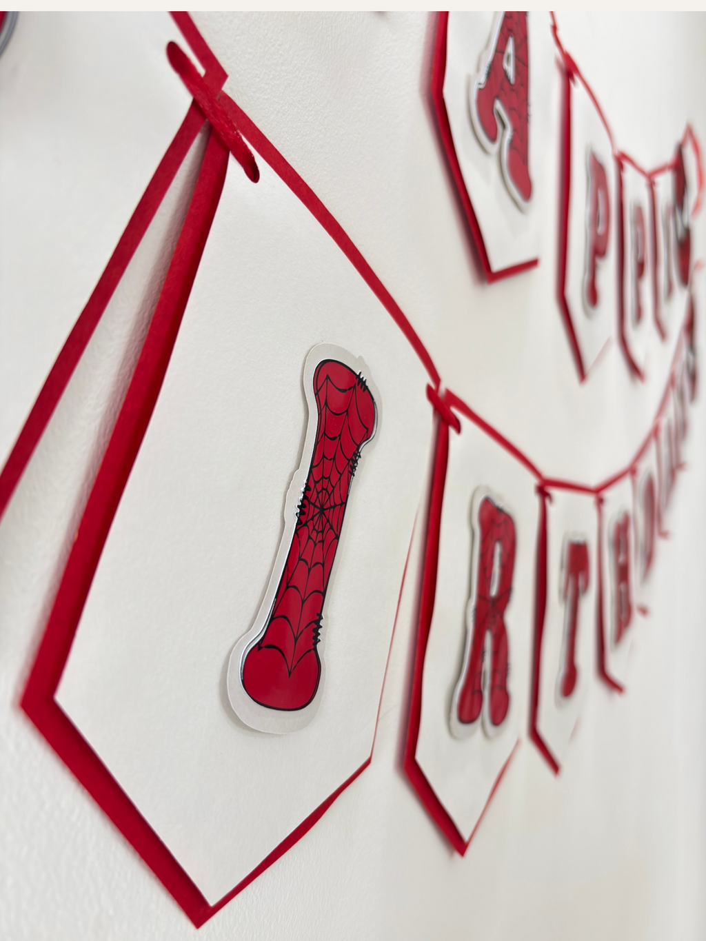 Paper Party Studio red and white swallowtail birthday banner with black spider-web lettering and hero theme details.