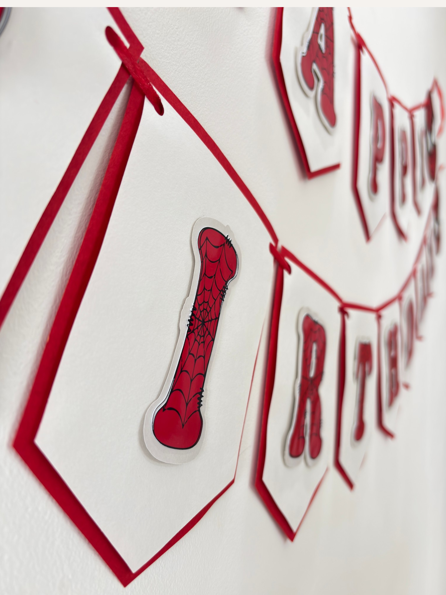 Paper Party Studio red and white swallowtail birthday banner with black spider-web lettering and hero theme details.