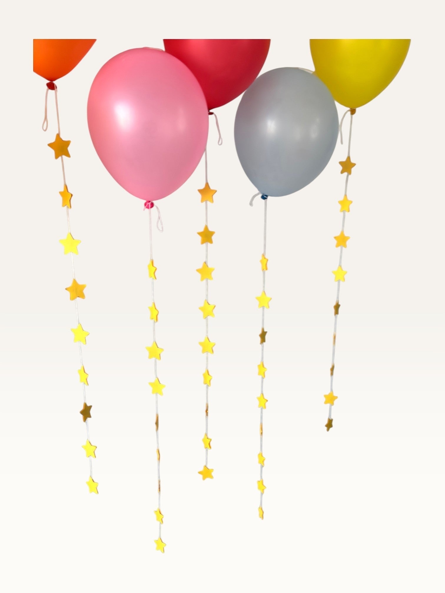 Paper Party Studio set of 10 yellow paper star garland strings hanging as decorative tails from colorful balloons.