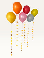Paper Party Studio set of 10 yellow paper star garland strings hanging as decorative balloon tails for celebrations.