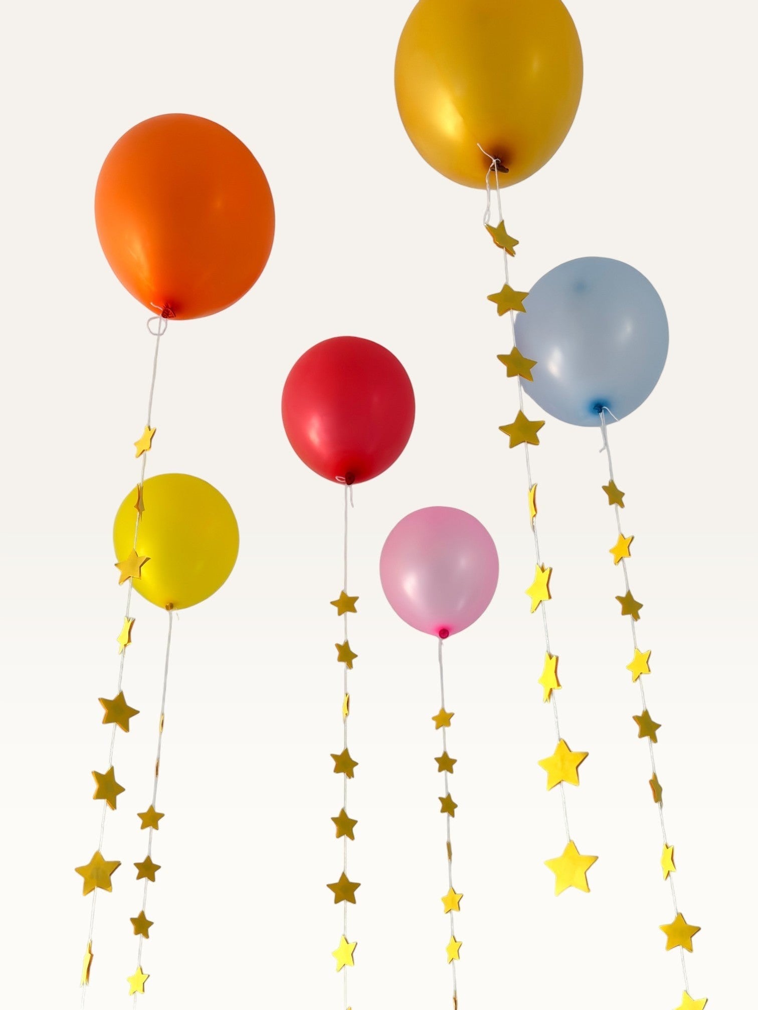 Paper Party Studio set of 10 gold paper star garland strings hanging as decorative tails from colorful balloons.
