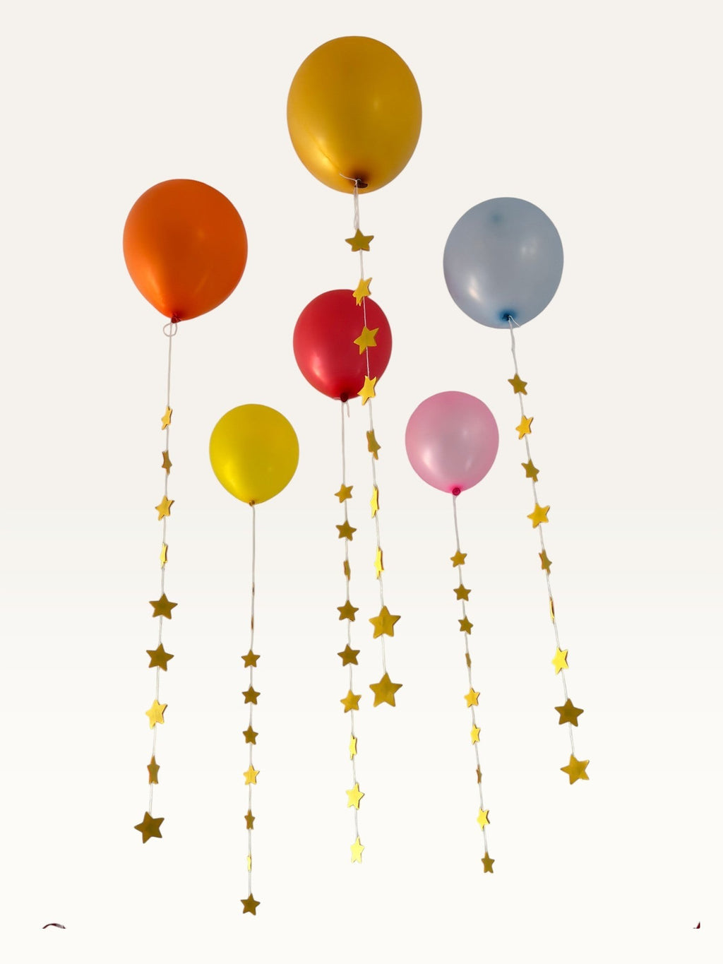 Paper Party Studio set of 10 yellow paper star garland strings hanging as decorative tails from colorful balloons.