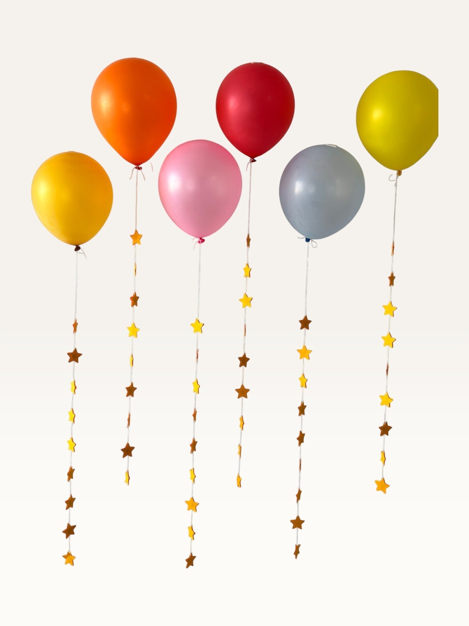 Paper Party Studio set of 10 yellow paper star garland strings hanging from colorful party balloons