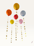Paper Party Studio set of 10 yellow paper star garland strings hanging as decorative tails from colorful balloons.