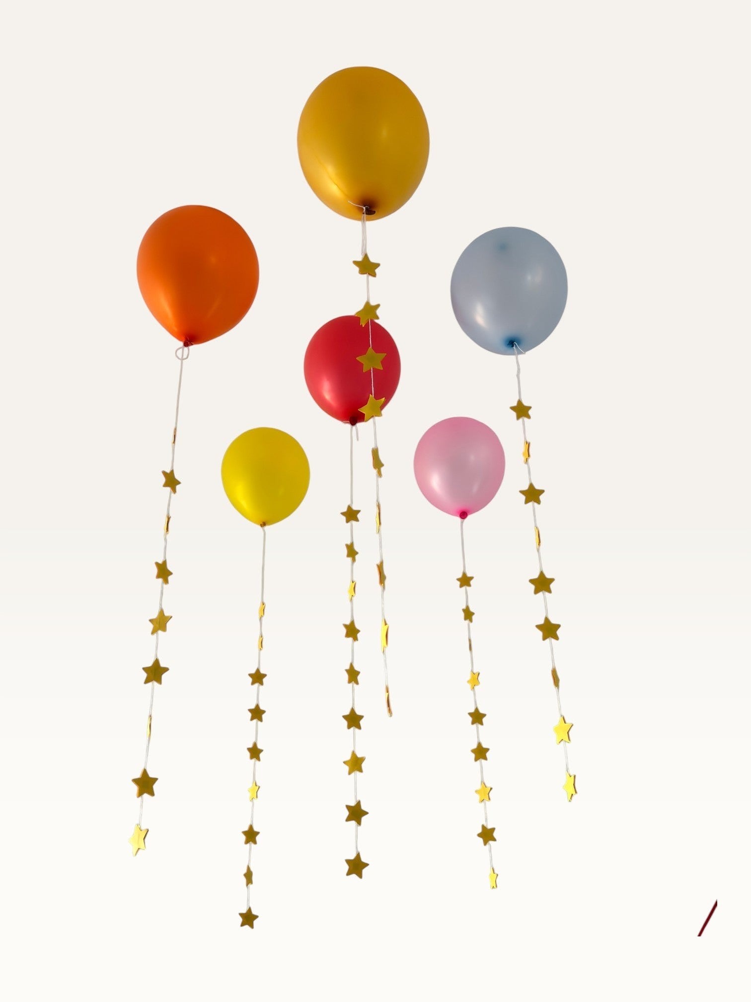 Paper Party Studio set of 10 yellow paper star garland strings hanging as decorative tails from colorful balloons.