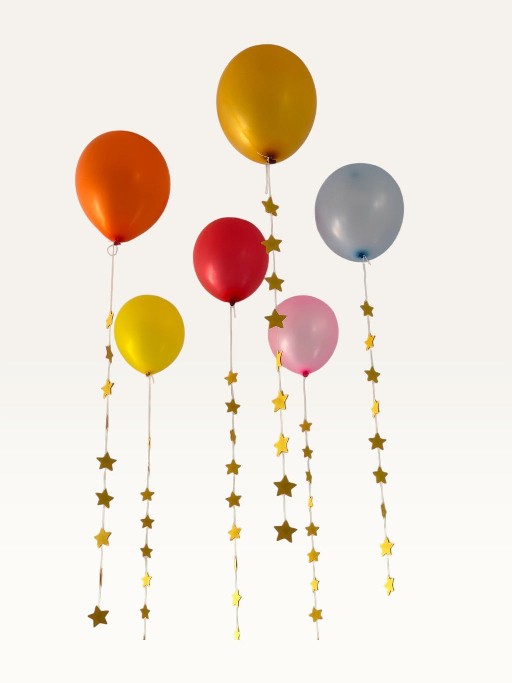 Paper Party Studio set of 10 yellow paper star garland strings hanging as decorative tails from colorful balloons.