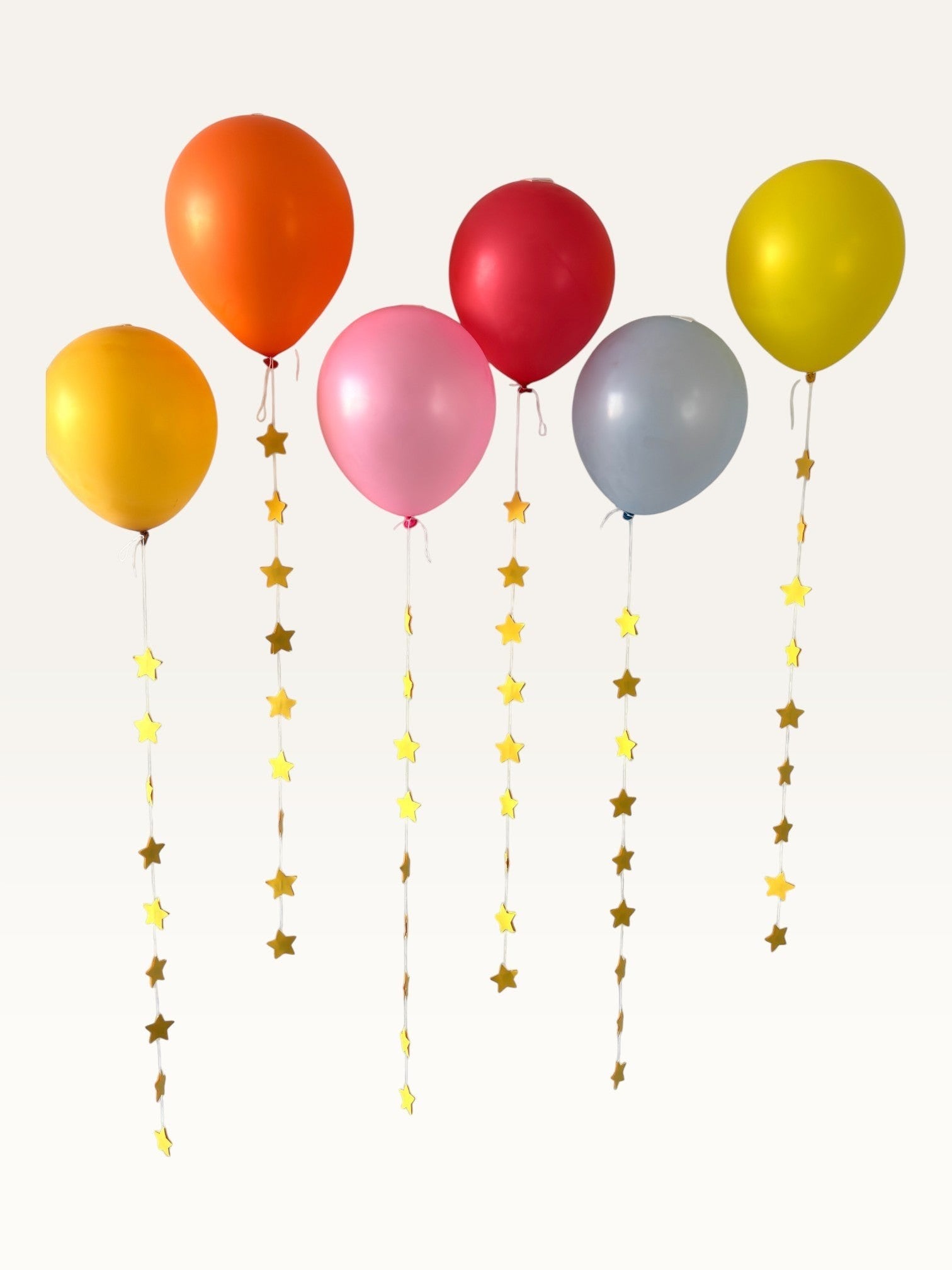Paper Party Studio set of 10 yellow paper star garland strings hanging from colorful party balloons