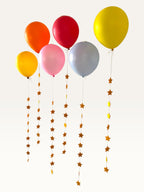 Paper Party Studio set of 10 yellow paper star garland strings hanging from colorful party balloons