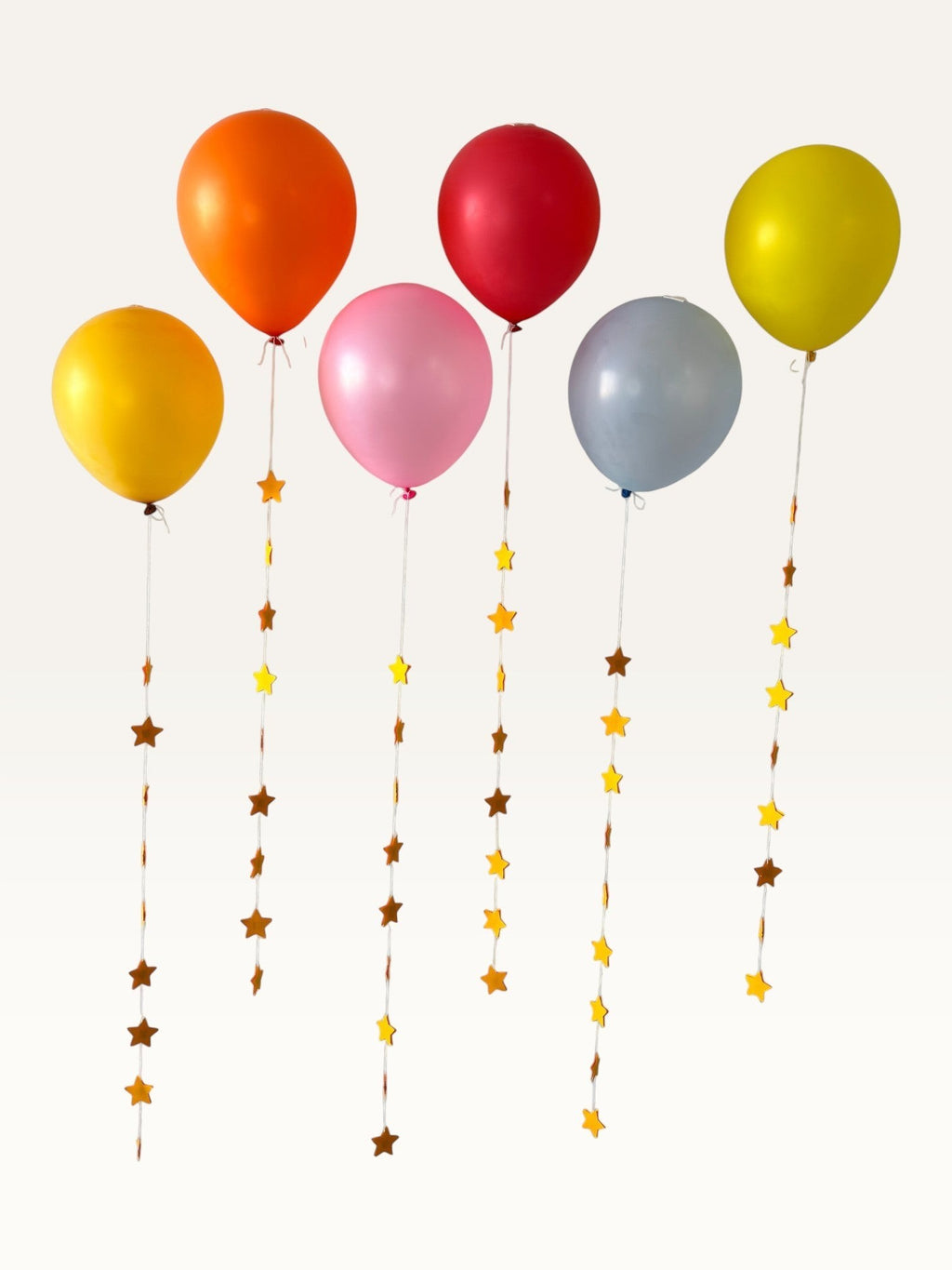 Paper Party Studio set of 10 yellow and dark yellow paper star garland strings hanging from colorful party balloons.