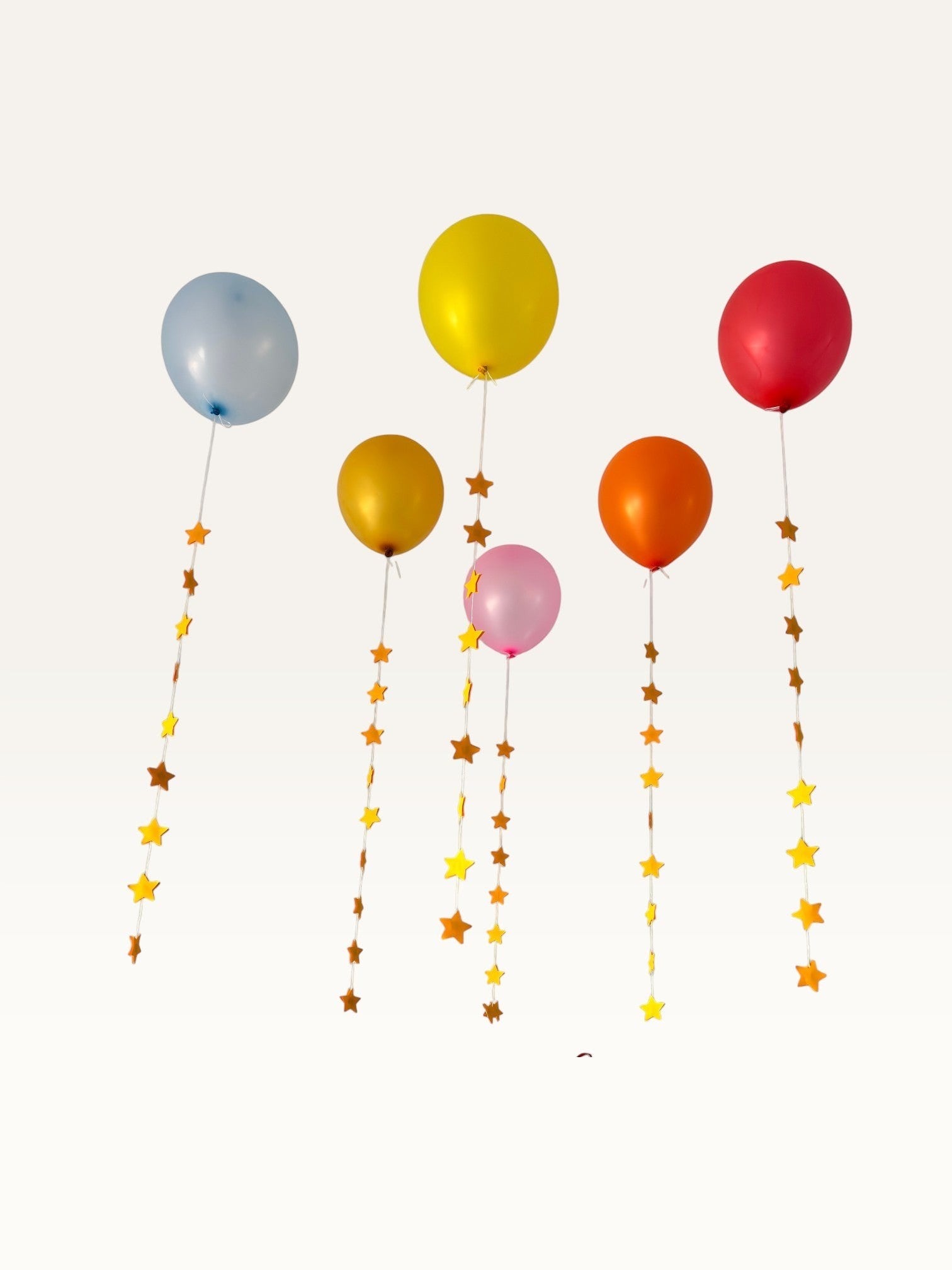 Paper Party Studio set of 10 yellow paper star garland strings hanging from colorful party balloons