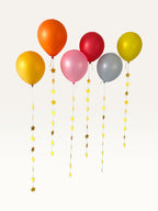 Paper Party Studio set of 10 yellow paper star garland strings hanging from colorful party balloons